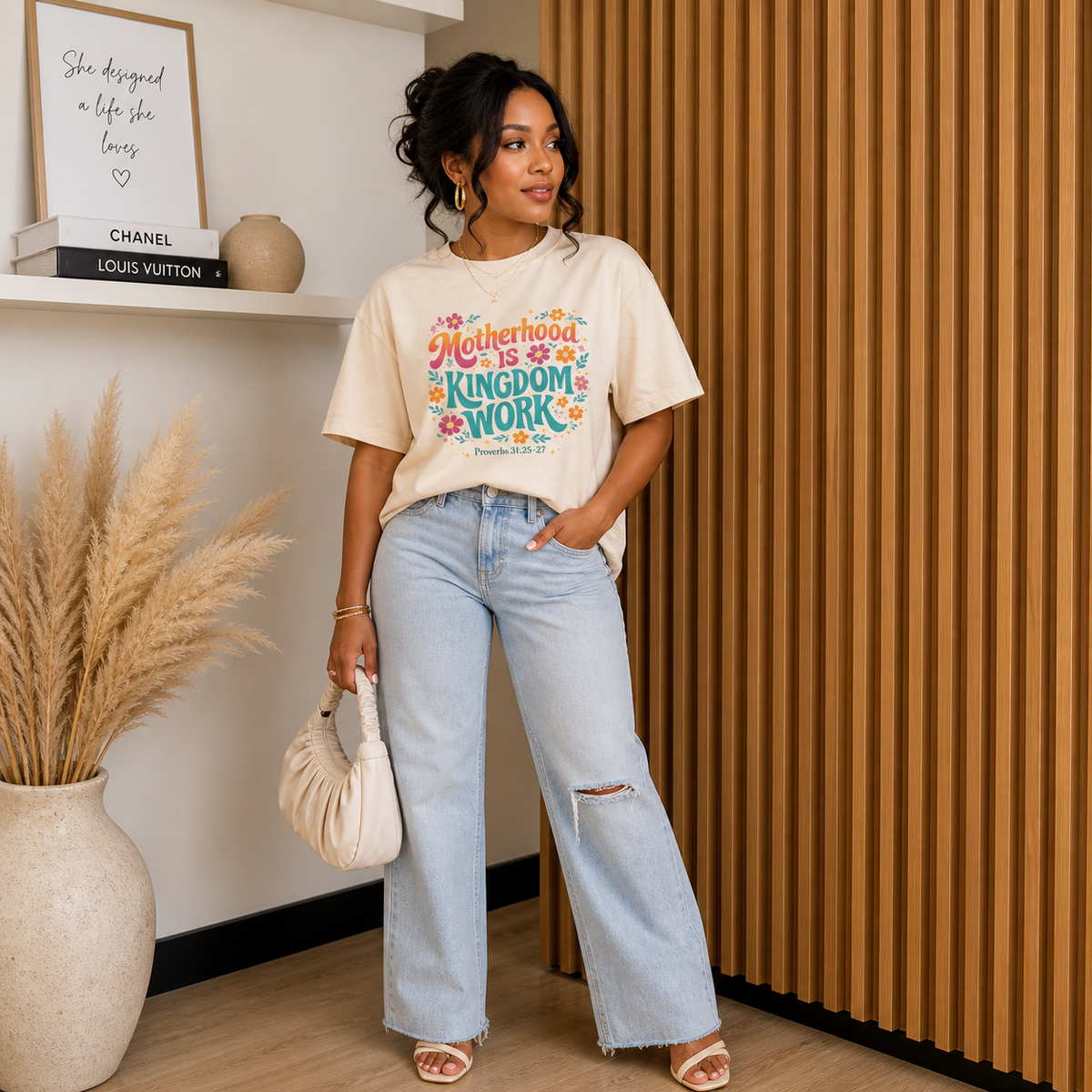 black woman posing wear an ivory shirt with colorful text that reads Motherhood Is Kingdom Work