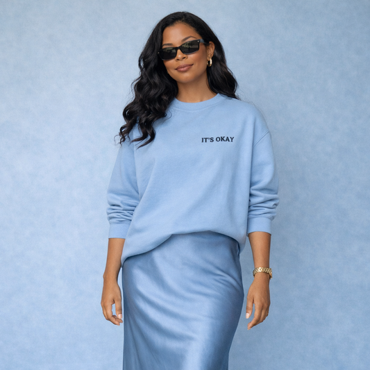 African American woman wearing blue It’s Okay crewneck sweatshirt styled with satin skirt and gold jewelry, elevated casual lifestyle outfit
